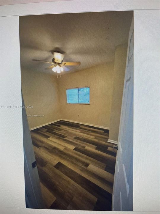 Interior room featuring wood-finish flooring, a neutral wall palette, a single window, and a ceiling-mounted light fixture with a fan