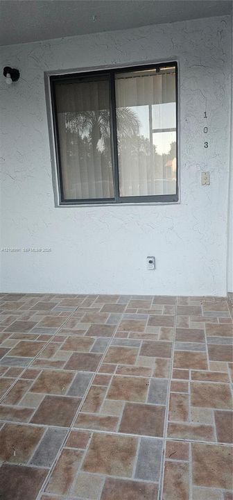 Covered exterior entryway featuring textured white stucco walls, multi-tonal decorative tile flooring, and a single-pane sliding window