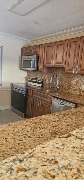 Kitchen featuring raised-panel wood cabinetry, natural stone countertops, stainless steel appliances, and an undermount sink with a gooseneck faucet