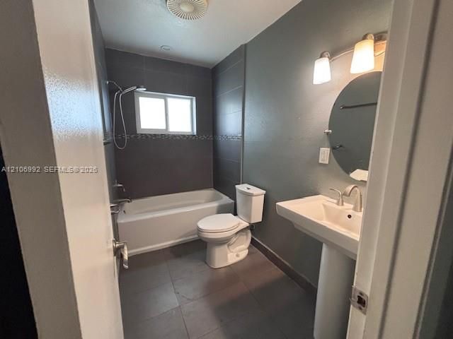 Bathroom featuring a pedestal sink, wall-mounted circular mirror, tile flooring, and a bathtub with a tiled surround