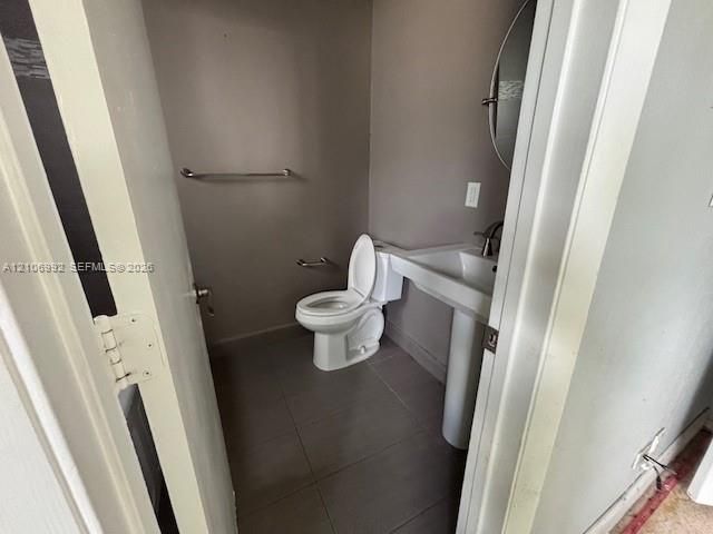 Pedestal sink with a single-handle faucet, circular wall-mounted mirror, ceramic tile flooring, and wall-mounted metal hardware