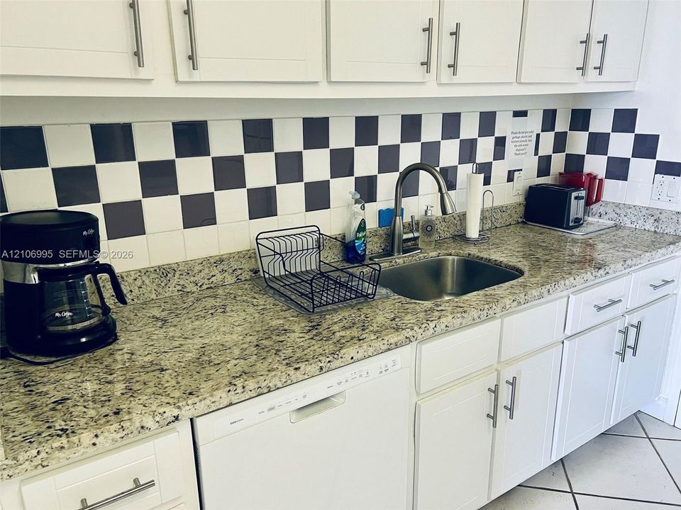 Kitchen featuring stone countertops, shaker-style white cabinetry with brushed-metal pulls, a stainless steel undermount sink, and a high-arch pull-down faucet