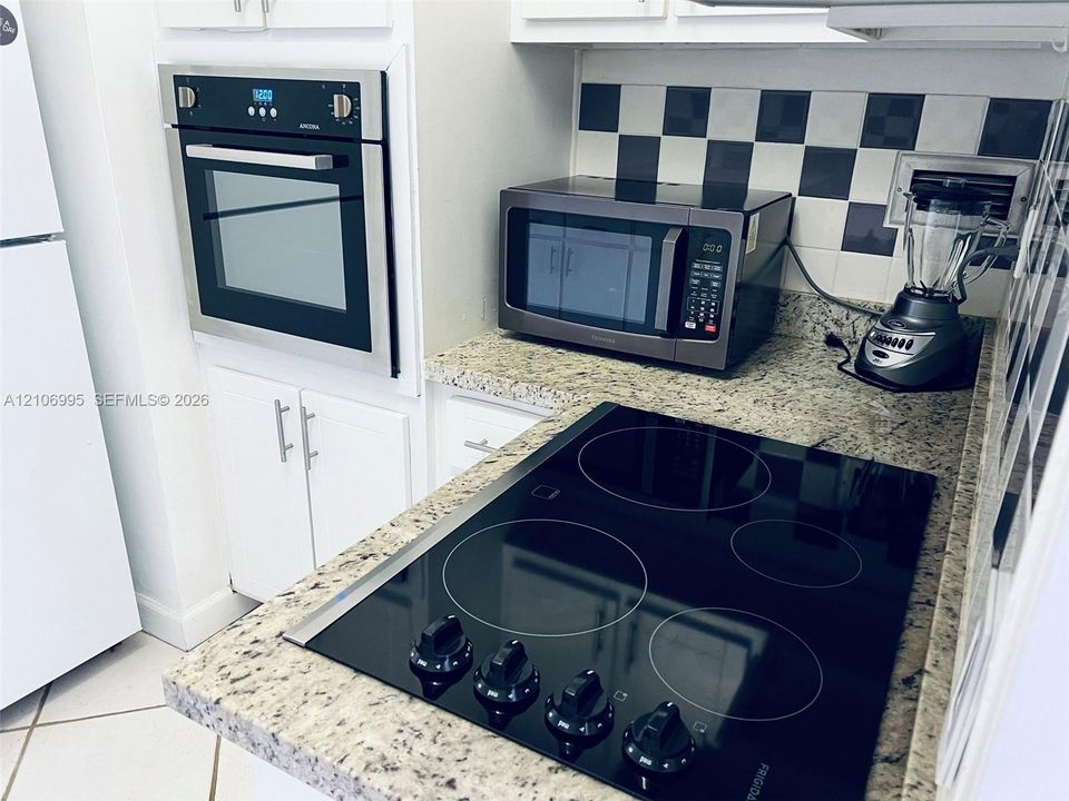 Kitchen featuring stone countertops, white cabinetry, a built-in wall oven, a glass-top electric cooktop, and a checkerboard-pattern backsplash