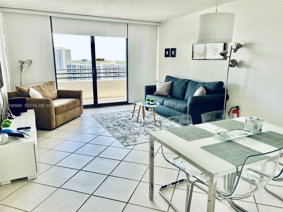 Open-concept living space featuring large-format ceramic tile flooring, floor-to-ceiling glass sliding doors, and a private balcony