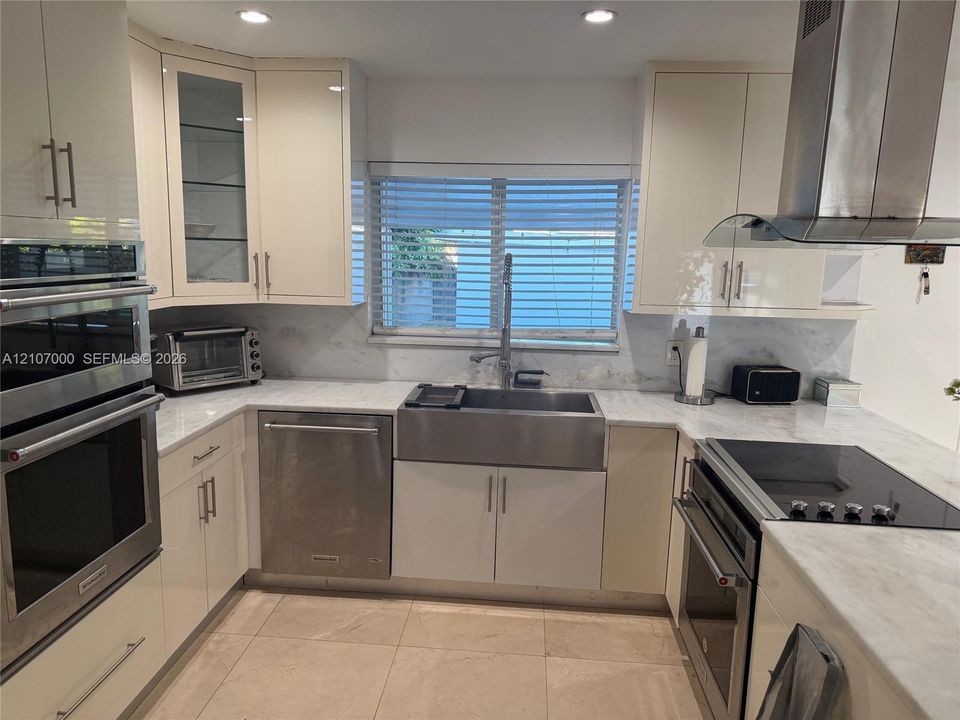 Kitchen featuring high-gloss cabinetry, stone-finish countertops, stainless steel farmhouse sink, built-in double wall oven, and a stainless steel range hood