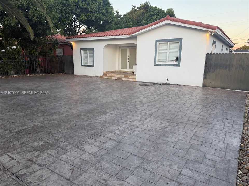 Stucco exterior with a terra cotta tile roof, expansive stamped concrete driveway, and recessed entryway featuring double glass-paneled doors