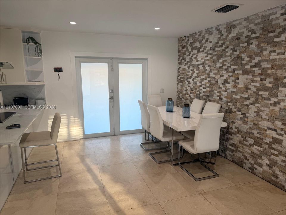 Stacked stone accent wall, dual-panel glass French doors, built-in open shelving, quartz countertop, and large-format tile flooring