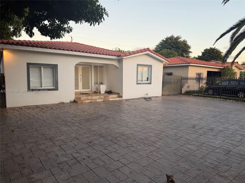 Stucco exterior with a red tile roof featuring an arched entryway, double-door main entrance, and an expansive stamped concrete driveway