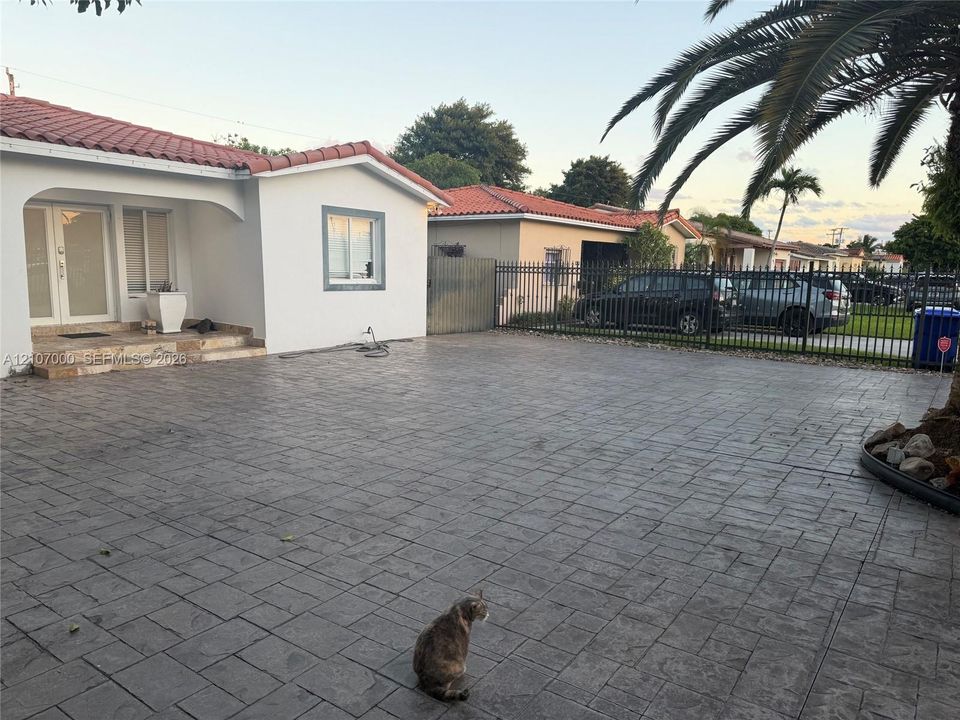 Stucco exterior with a terra cotta tile roof, expansive stamped concrete driveway, and black metal perimeter fencing