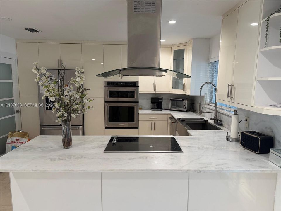 Contemporary kitchen featuring high-gloss cabinetry, stone-surface countertops, a stainless steel wall oven, an integrated cooktop, and a stainless steel range hood