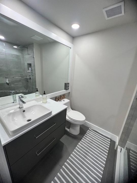 Floating vanity featuring two drawers, a rectangular vessel sink with a chrome faucet, a stone-composite countertop, and a large wall-mounted mirror