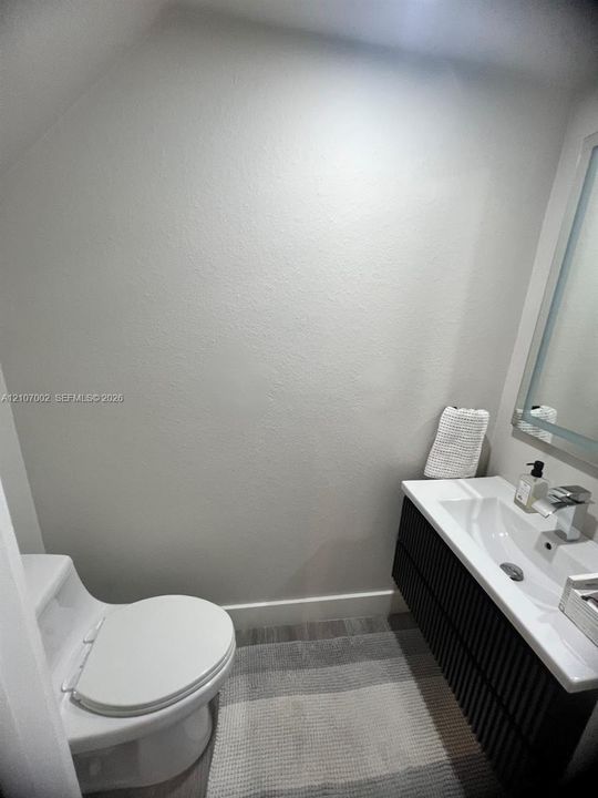 Wall-mounted, dark-toned textured vanity with integrated rectangular sink and polished chrome faucet, paired with a white porcelain commode and rectangular wall mirror