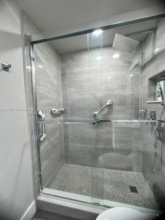 Walk-in shower with floor-to-ceiling large-format tile, frameless glass enclosure, rainfall shower head, integrated wall niche, and hexagonal tile flooring