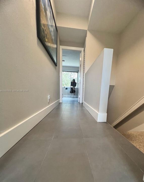 Hallway featuring large-format grey tile flooring, neutral wall paint, and partial stairwell wall