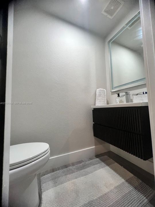 Wall-mounted vanity featuring a ribbed black finish, white countertop, integrated basin, and a rectangular LED-backlit mirror