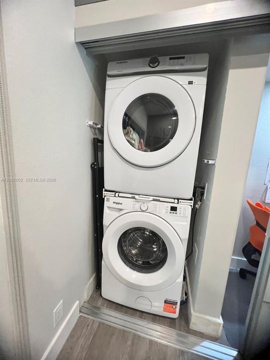 Stacked laundry center featuring a front-loading washer and electric dryer set within a dedicated recessed closet area