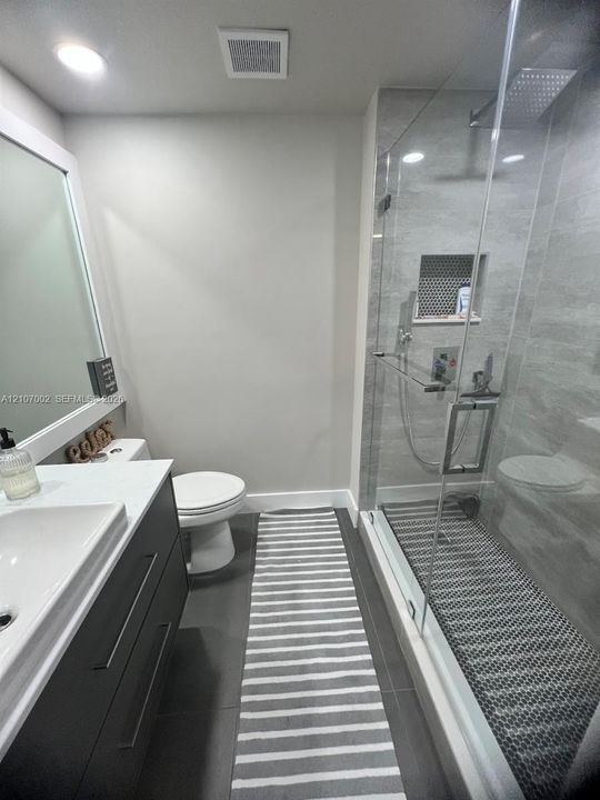 Modern vanity with a rectangular basin, quartz countertop, glass-enclosed shower with a rainfall showerhead, and a tiled shower niche