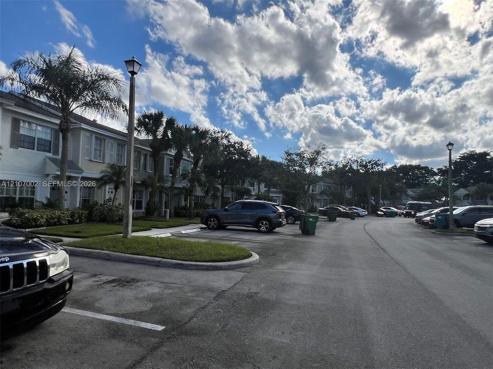 Multi-story residential exteriors featuring neutral siding, shuttered windows, paved parking area, and manicured landscaping with palm trees