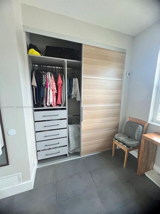 Closet featuring wood-finish sliding doors, built-in shelving, and integrated five-drawer dresser with matte hardware