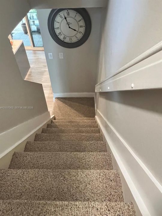 Staircase featuring wall-mounted lighting, neutral carpeting, and millwork detail