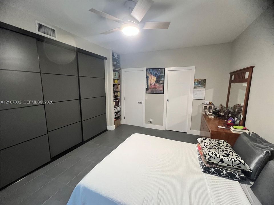 Large-scale sliding door closet with matte finish, ceramic tile flooring, built-in floor-to-ceiling shelving, and a modern ceiling fan with integrated lighting