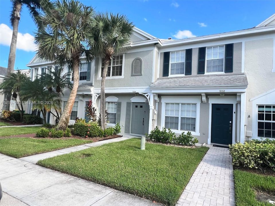 Stucco exterior featuring multi-paned windows, shutter accents, and paver walkways