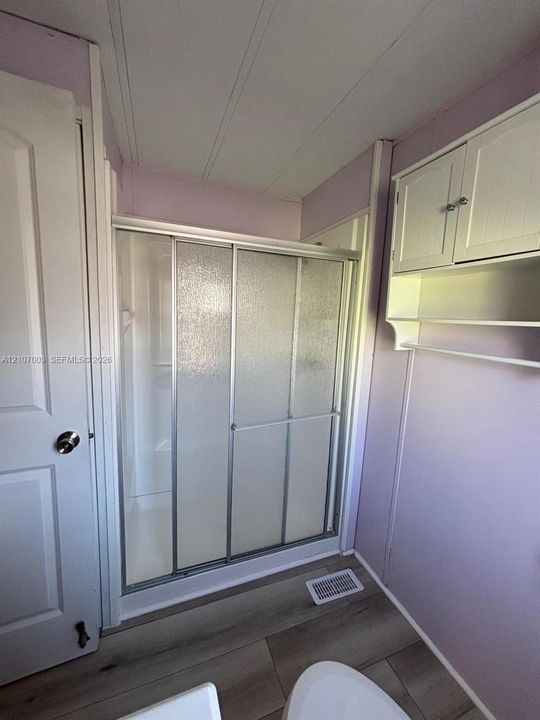 Walk-in shower with textured glass sliding doors, wood-finish flooring, and built-in white wall cabinetry with integrated shelving