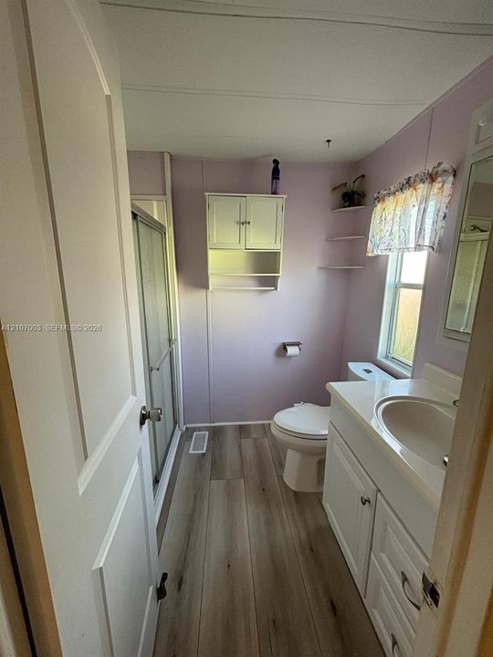 Bathroom featuring wood-finish flooring, a white vanity with an integrated sink, a walk-in shower with a glass enclosure, and wall-mounted white cabinetry