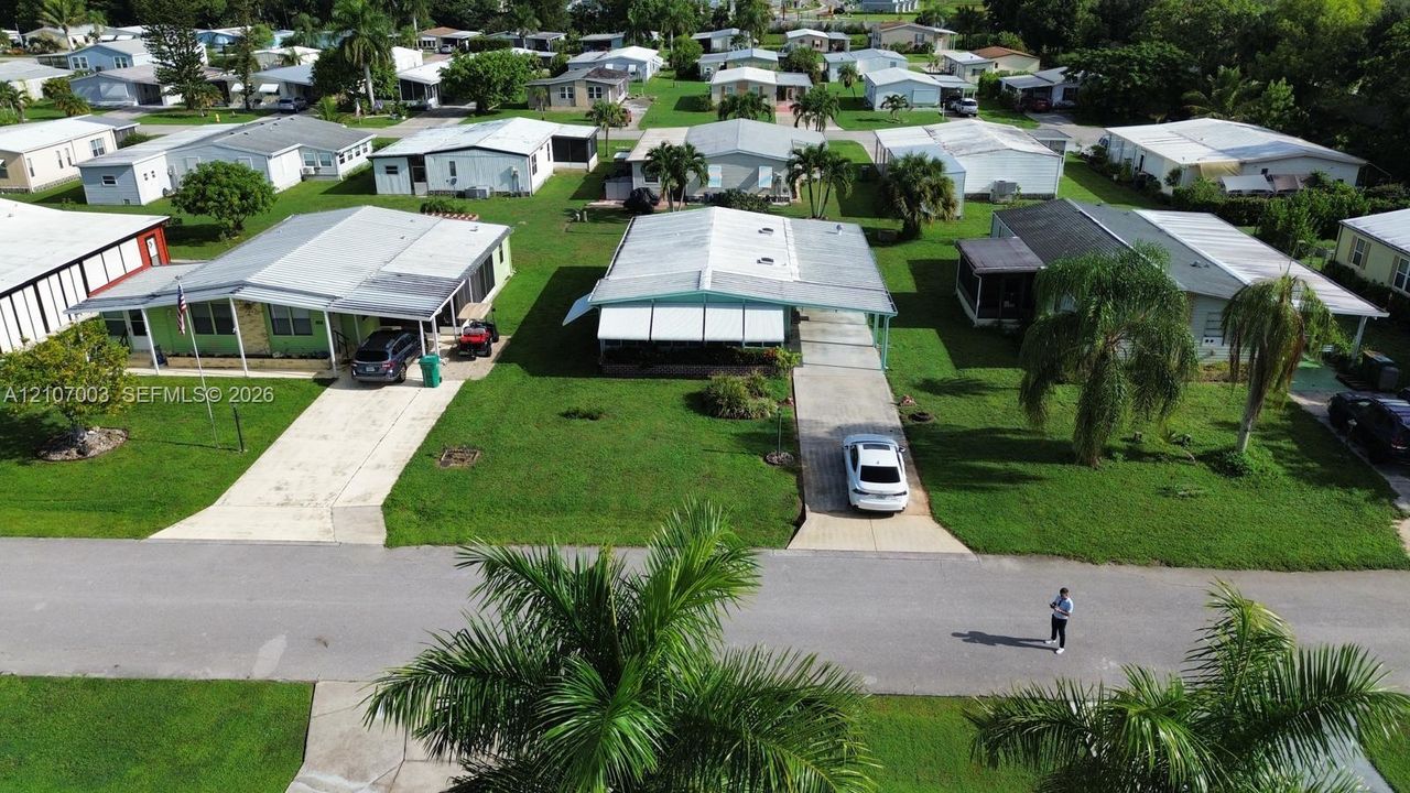 Aerial perspective featuring a manicured lawn, concrete driveway, attached covered carport, and mature palm trees