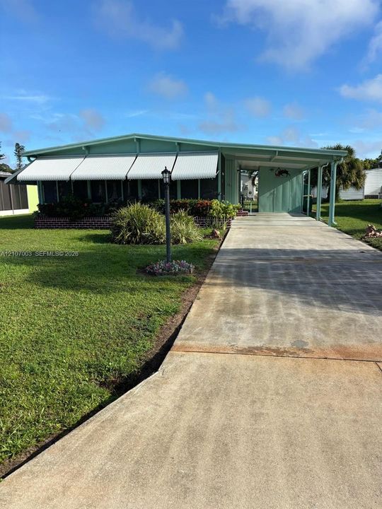 Exterior featuring a concrete driveway, attached carport, screened-in porch, metal window awnings, and a brick-bordered garden bed