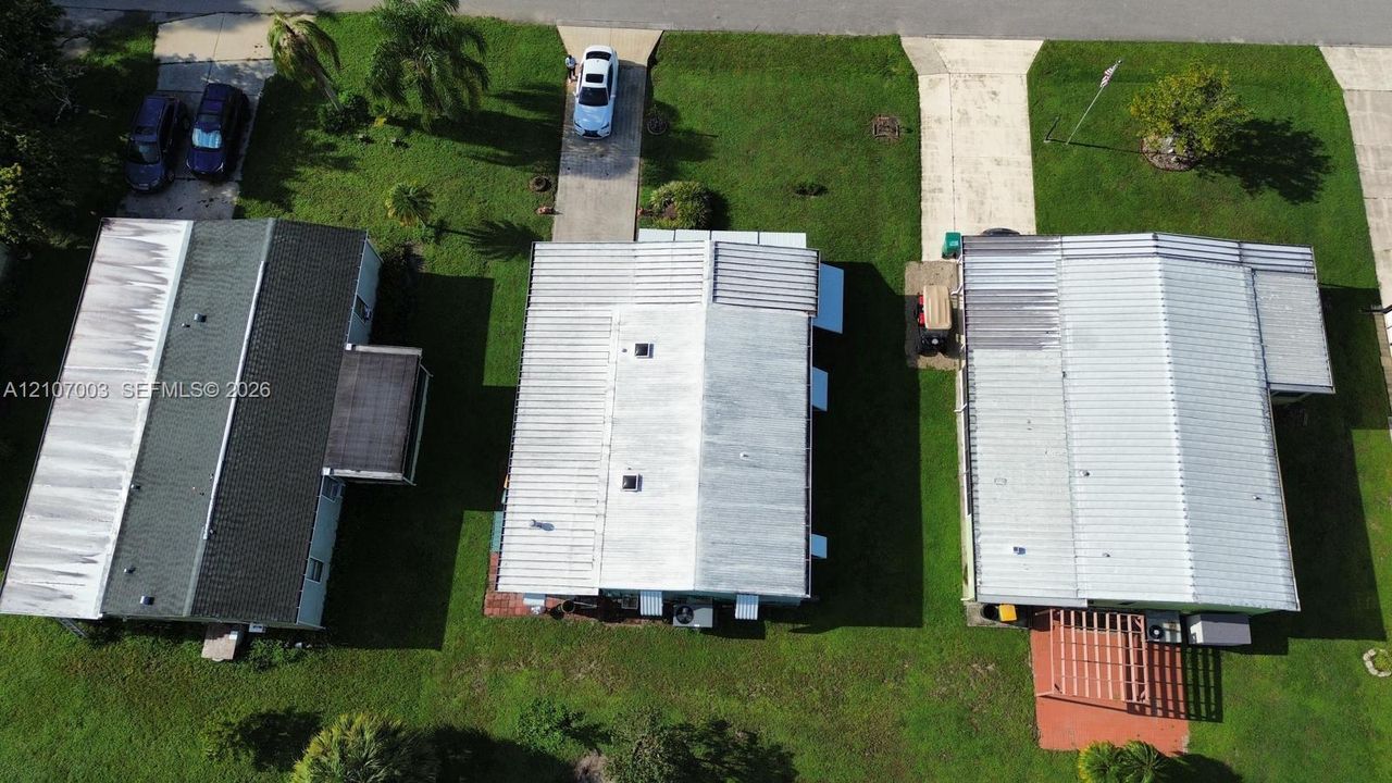 Aerial perspective featuring a metal roof, concrete driveway, and grassy lot