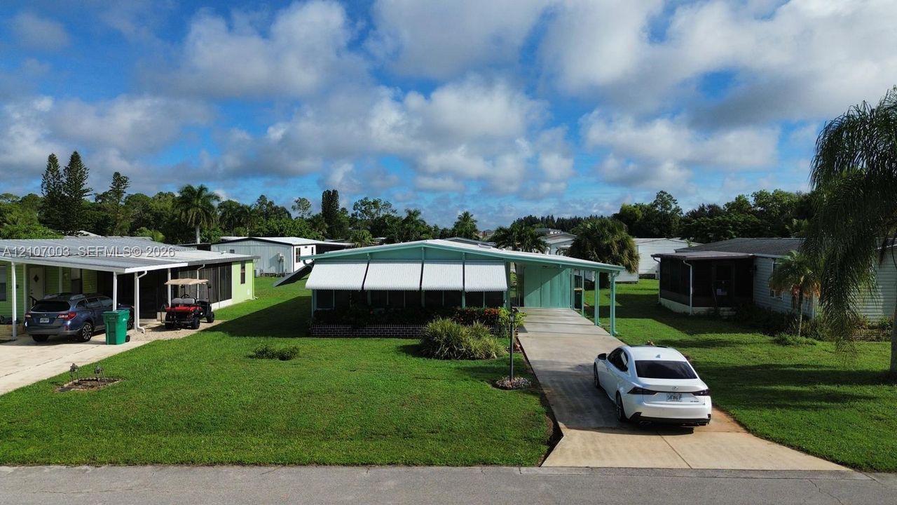 Single-story residence featuring a low-slope roof, metal window awnings, a side-entry carport, and a concrete driveway