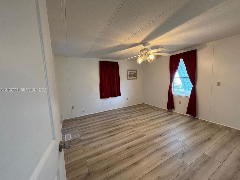 Room featuring wood-finish flooring, white wall panels, and a central ceiling fan with integrated lighting