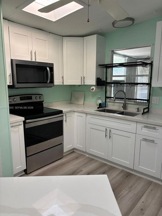 Kitchen featuring white shaker-style cabinetry, stainless steel appliances, solid-surface countertops, dual-basin sink, and wood-finish flooring