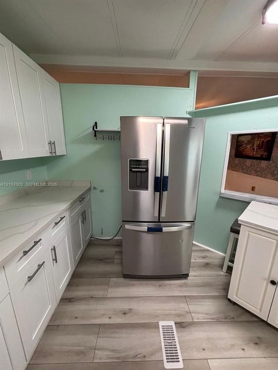 Kitchen featuring white shaker-style cabinetry, light-toned countertops with veining, stainless steel French door refrigerator, and wood-finish flooring