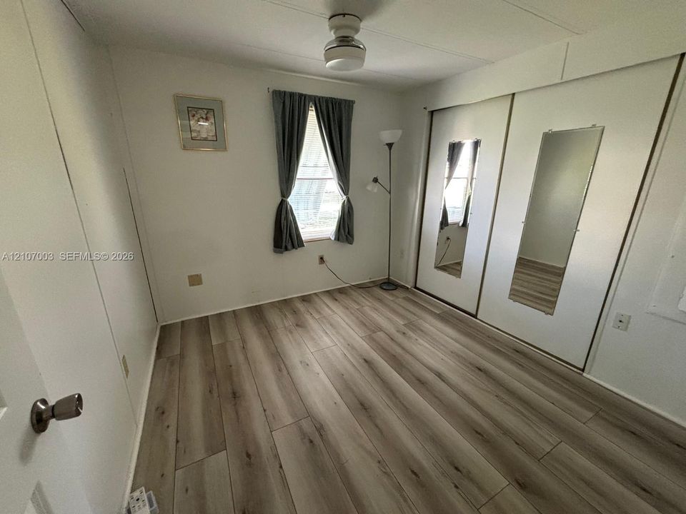 Room featuring wood-finish flooring, dual sliding-door closets with integrated mirrors, and a ceiling-mounted light fixture