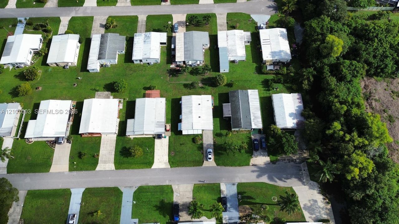 Aerial view of a residential neighborhood featuring paved streets, dedicated driveways, manicured green space, and bordering mature tree canopy