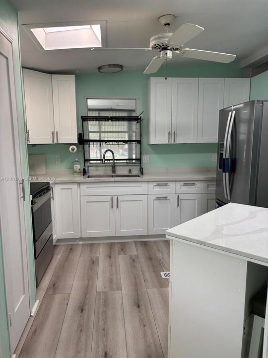 Kitchen featuring white shaker-style cabinetry, stainless steel appliances, wood-finish flooring, quartz-surfaced countertops, and a skylight