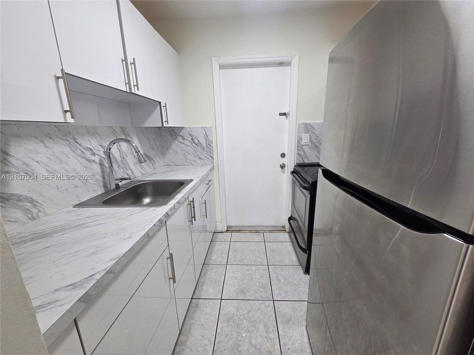 Kitchen featuring high-gloss white cabinetry, stone-patterned laminate countertops, stainless steel refrigerator, and ceramic tile flooring