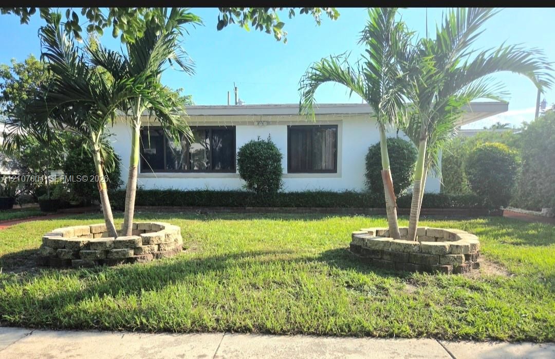 Exterior featuring a white stucco facade, stacked stone circular planters, palm trees, and dark-frame windows
