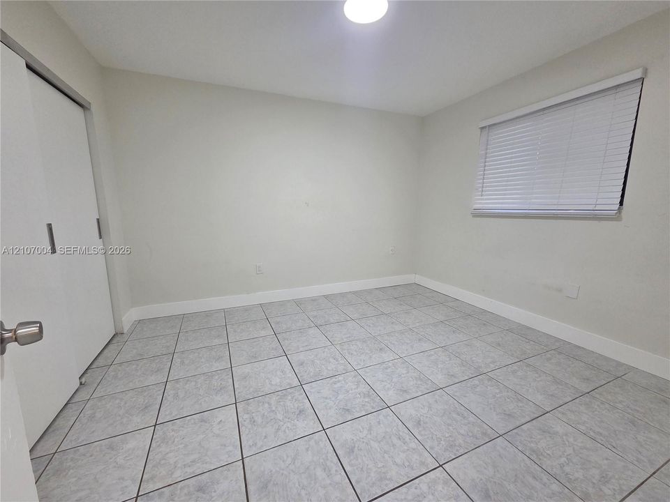 Neutral-toned room featuring large-format square tile flooring, a dual-panel closet door, and a horizontal slatted window blind
