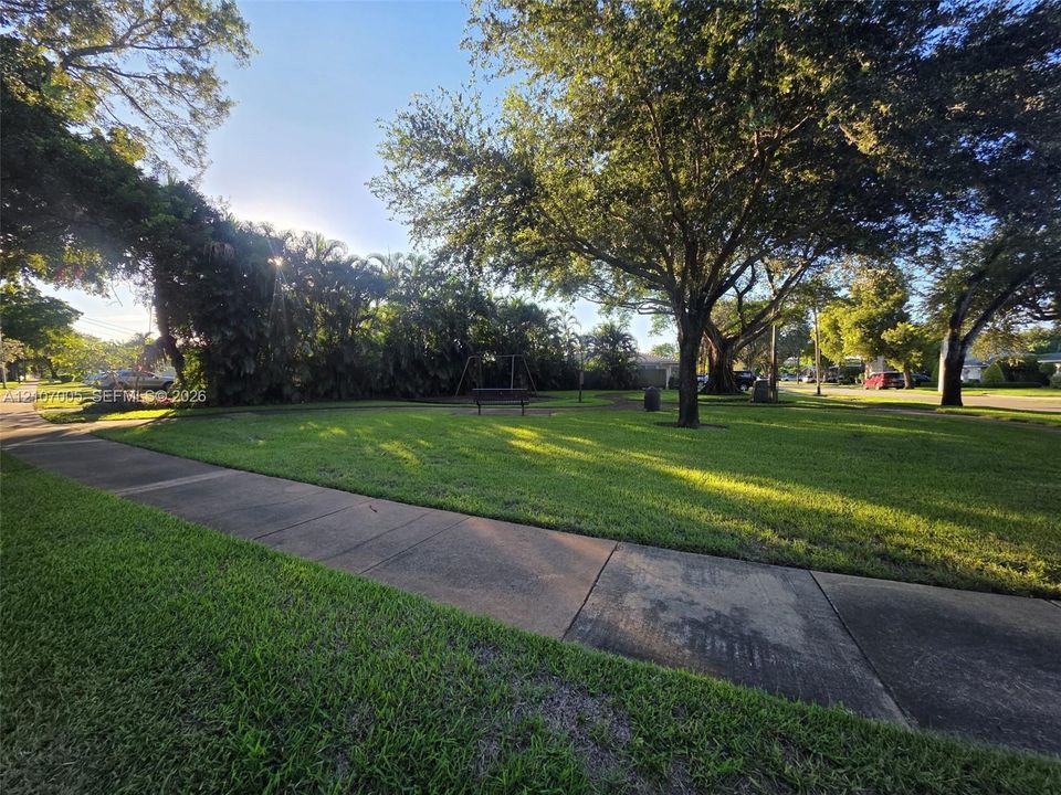 Expansive green space featuring mature trees, a concrete pathway, and established landscaping