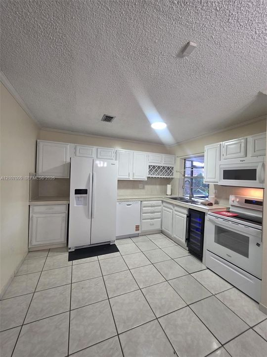 Kitchen featuring white cabinetry, integrated wine storage, tiled flooring, and a suite of white appliances