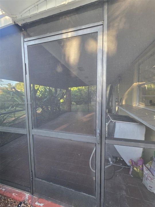 Screened enclosure featuring metal-framed door, tile flooring, and a pass-through service shelf