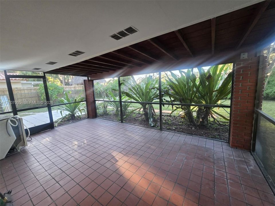 Screened-in porch featuring a tiled floor, exposed wood beam ceiling, red brick column accents, and aluminum framing