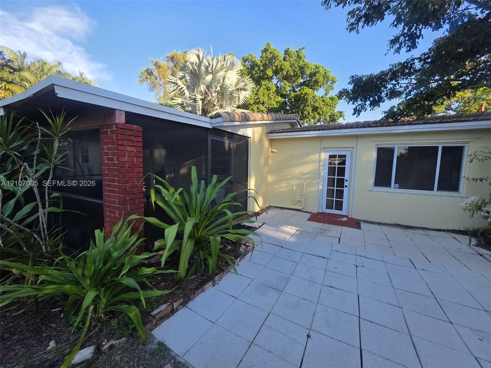 Exterior patio featuring large-format concrete pavers, a screened-in porch with exposed brick column, and a glass-paneled entry door