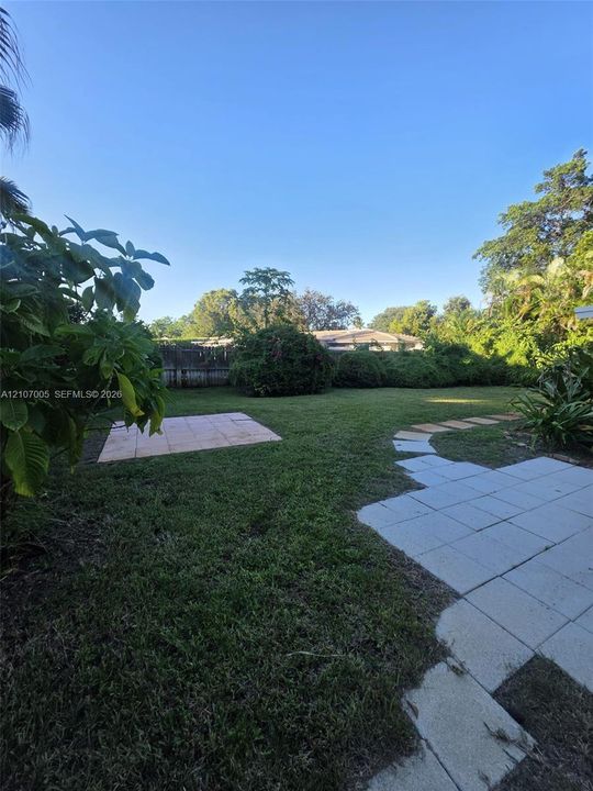 Backyard featuring a grass lawn, stone paver patio areas, stone stepping stones, mature perimeter vegetation, and a wood privacy fence