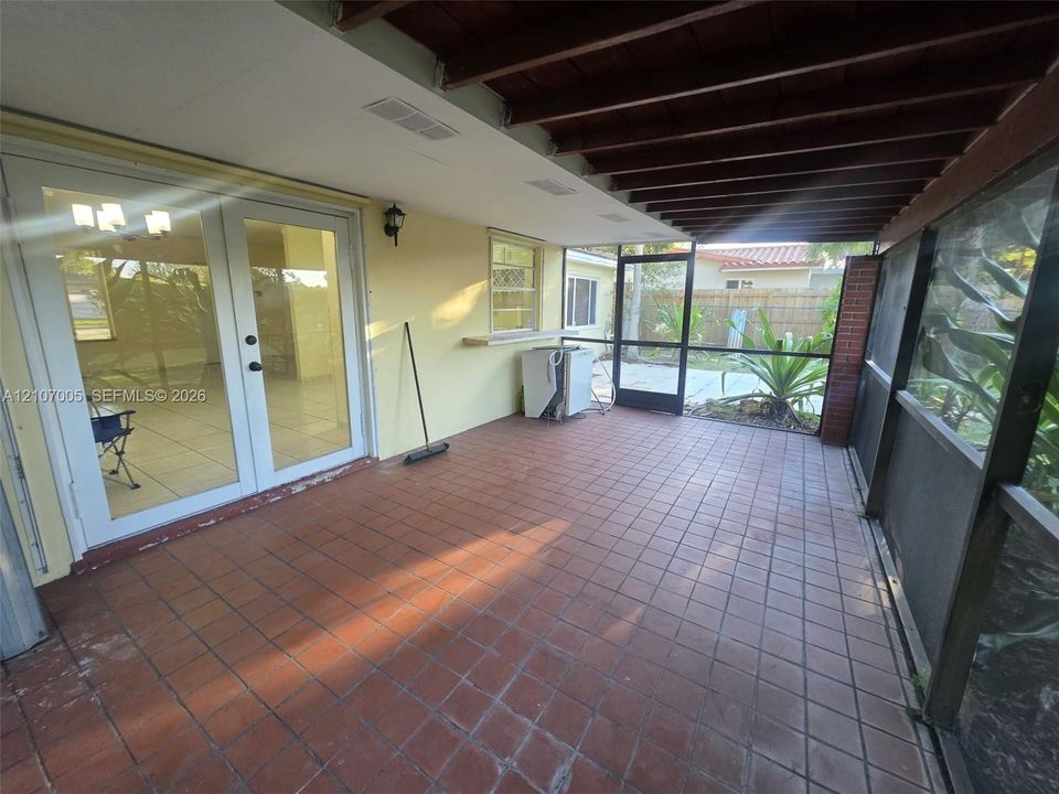 Screened-in patio featuring terra-cotta tile flooring, exposed wood-beam ceiling, brick pillar accents, and glass-paneled double doors