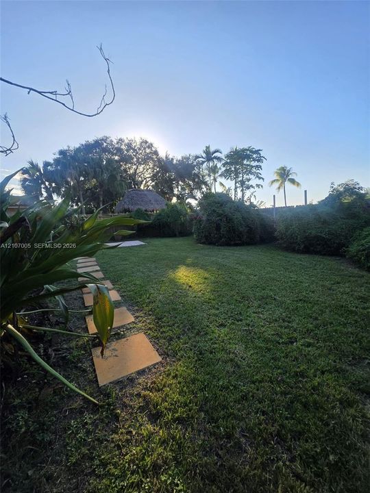 Expansive lawn with stone paver walkway, mature landscaping, and a detached thatched-roof structure