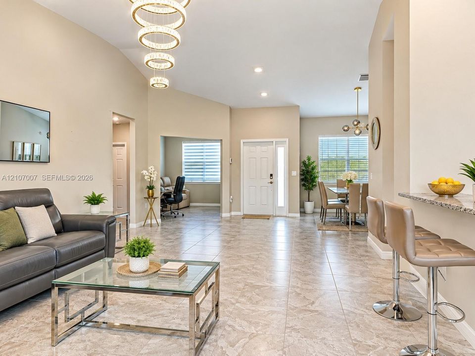Vaulted ceilings, tile flooring, multi-tiered ring chandelier, built-in breakfast bar with stone-finish countertop, and recessed lighting
